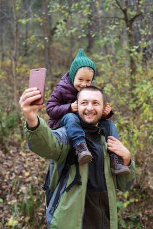 Man taking a selfie with his daughter in an autumn forest. Soft focus on a man's face.の写真素材