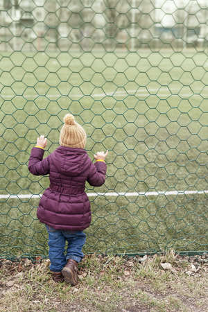 Little girl looking at the playing-field through grateの写真素材