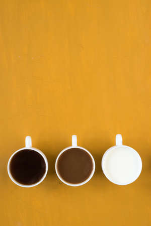 Three cups with coffee and milk on yellow backgroundの写真素材