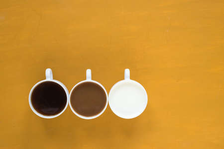 Three cups with black coffee, coffee with milk and just milk on yellow background.の写真素材