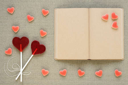 Two lollipops in the shape of a heart placed near an old diary with blank pages. There are also heart-shaped fruit candies all around. Saint Valentine's Day, copy space.の写真素材