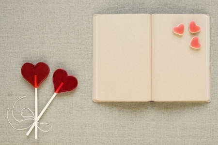 Two lollipops in the shape of a heart placed near an old diary with blank pages. There are also heart-shaped fruit candies all around. Saint Valentine's Day, copy space.の写真素材