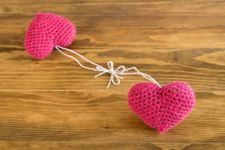 Two crocheted hearts tied together on a wooden tableの写真素材