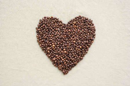 Heart made of coffee beans on a grey tissue background shot overhead.の写真素材