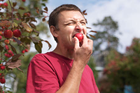 Young man eating a small red appleの写真素材
