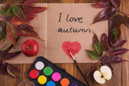 Autumn composition with leaves, apples, water-colours and a sketch book with a sign I love autumn and heart in it.の写真素材