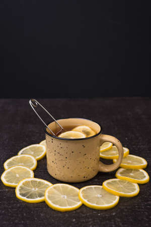 Big yellow mug with lemon tea and lemon circles on a black shabby background.の写真素材