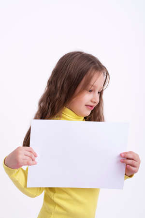 5-year-old girl with long wavy hair holding a blank sheet of paper.の写真素材