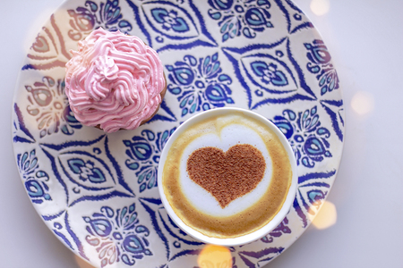 cappuccino heart in a white cup with a cupcake and creamの写真素材