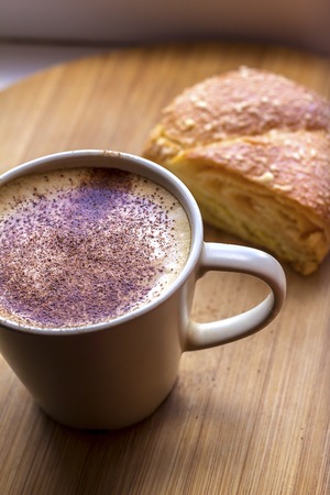 a cup of cappuccino coffee with a fragrant hot bunの写真素材