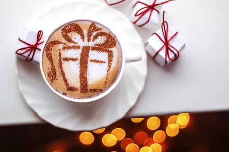 Christmas coffee in a white cup with a gift picture on white foamの写真素材