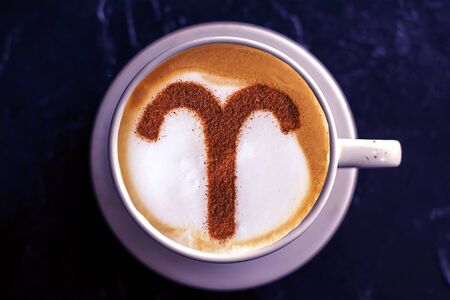 zodiac sign Aries on a foam of hot cappuccino in a white cup and stars on a dark table
