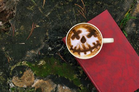 Coffee cup as jack o lantern pumpkin on wooden table over autumn backgroundの写真素材