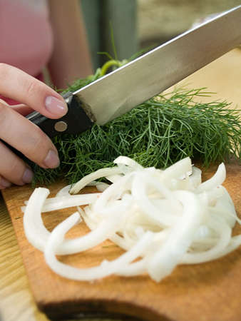 female hand holding knife above board with dil and onionの写真素材