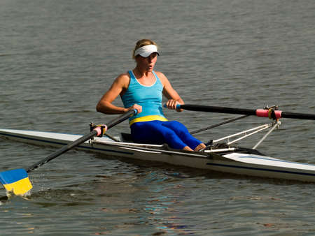 Sporty young lady rowing in boat on water