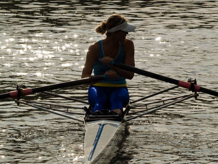 Sporty young lady rowing in boat on water duskの写真素材