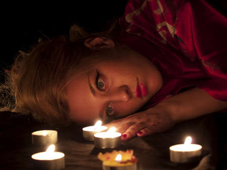 Beautiful blonde lady with oriental make-up lying in candlesの写真素材