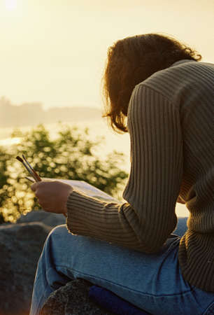 Female painter with brushes sits on rock in sunriseの写真素材