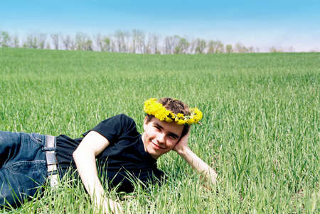 Young man in dandelion crown laying in field in summerの写真素材