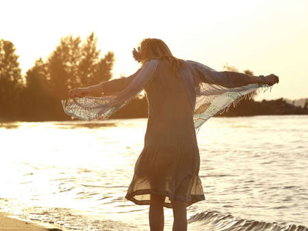 Blonde beautiful lady with fabric on shore in sunsetの写真素材