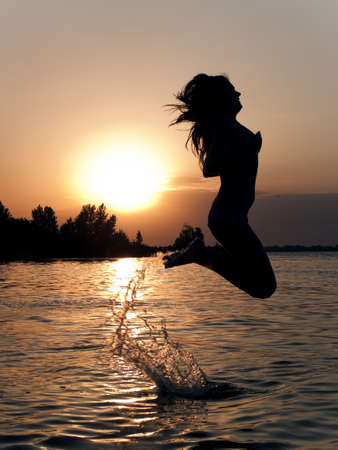 Lady in bikini jumping above water on sunsetの写真素材