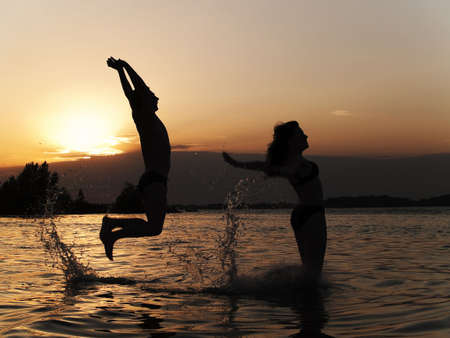 Active couple jumping into water on sunsetの写真素材