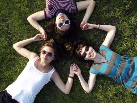 Three young girls laying on grass smilingの写真素材