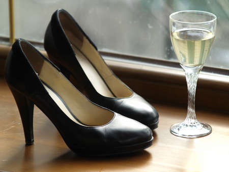 Pair of female shoes on heels and a glass of wine on windowの写真素材