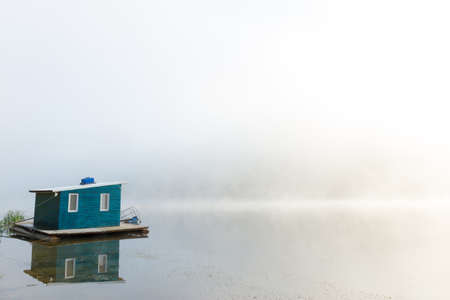 Floating lakehouse on calm foggy river at dawnの写真素材