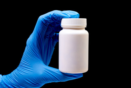 Medical pills in white jar on an isolated black background with reflection in hand natural organic...