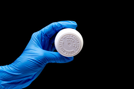 Medical pills in white jar on an isolated black background with reflection in hand natural organic...