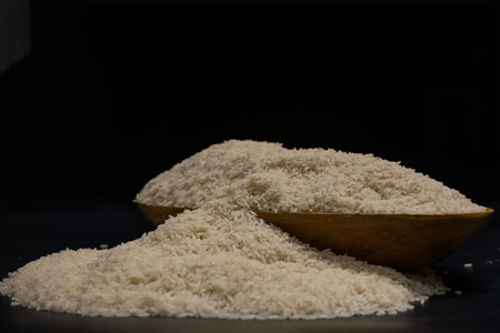 Uncooked indian jasmine rice in wooden bowl on black background