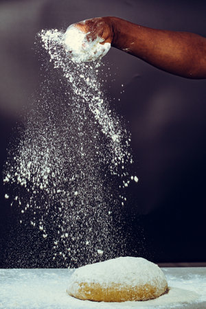 Close-up image of a man's hand sprinkling flour on a dough.の写真素材