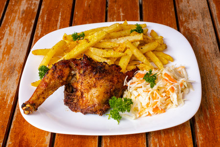 Grilled chicken leg with french fries and coleslaw on wooden tableの写真素材
