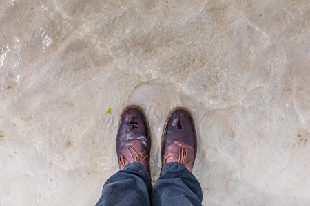 Top view of male legs in brown shoes standing on the sand.