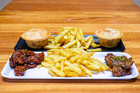 Fast food on a wooden table. French fries, grilled meat, sauce and bread.