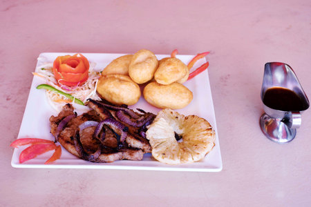 Fried meat with vegetables and sauce on a white plate in a restaurantの写真素材