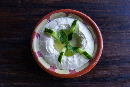 Cucumber yogurt with mint leaves in a bowl on a wooden backgroundの写真素材