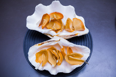 Seashells with rose petals on a black plate.