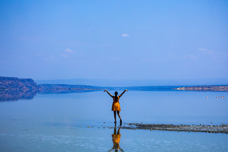 Girl in a yellow dress standing on the shore of the lake and raising her hands up