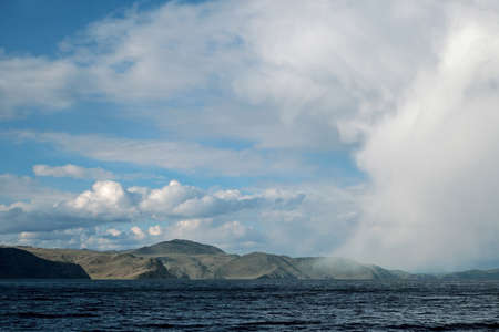 Big cloud in the form of man's face hangs down just over water and mountainsの写真素材