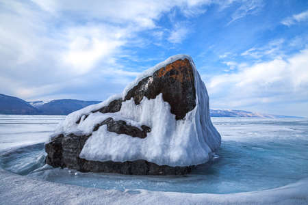 Big stone and melting ice in spring on background of blue sky and white cloudsの写真素材