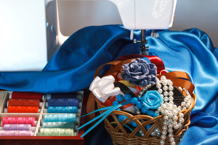 Sewing accessories, colorful thread spools, blue silk fabric, decorations and sewing machineの写真素材