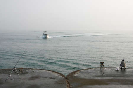 Fishermen with fishing rods on the city wharf nearby a seaの写真素材