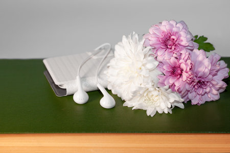 White and pink flowers of chrysanthemum, phone, earphones and old book on light background, romantic...