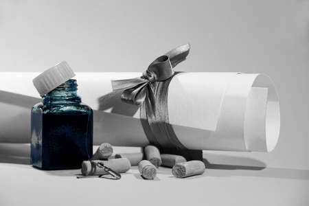 Scroll of white paper, ink bottle, pastel chalks and metal quills for fountain pen on light background, vintage image in soft grey tones with artistic toolsの写真素材