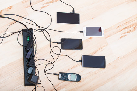 four smartphones and one classic phone connected to chargers