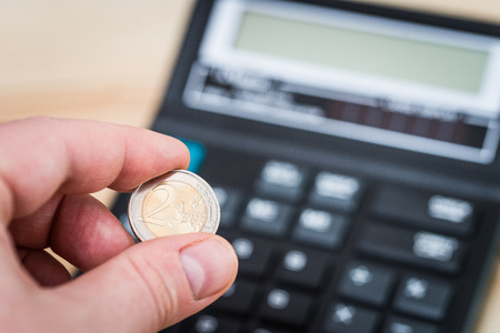 two euro coin in the man's hand - a calculator in the background two euro coin in the man's hand - a calculator in the background