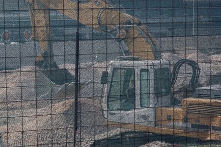 Excavator at construction site digging ground foundation behind plastic safety protective net. Selective focus background.の写真素材