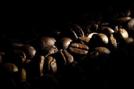 Coffee beans background. 
Brown texture of roasted coffee seeds filling all frame. 
Space for copy text.
Selective spot light, back light, shallow depth of field, selective focus. Extreme close up.の写真素材